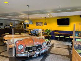 Ansicht TryOut Bar mit Autodekoration und Steinboden und TV. Im Hintergrund sieht man die Bar.