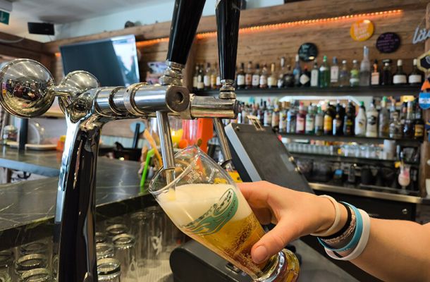 Ein Bier wird am Bierhahn gezapft. Im Hintergrund sieht man einen TV und das Spirituosen Angebot